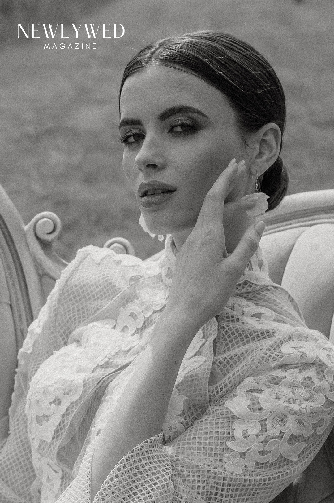 woman wearing a lace bridal gown posing on a velvet ornate sofa in a green grassed garden. Wearing white floral bridal earrings