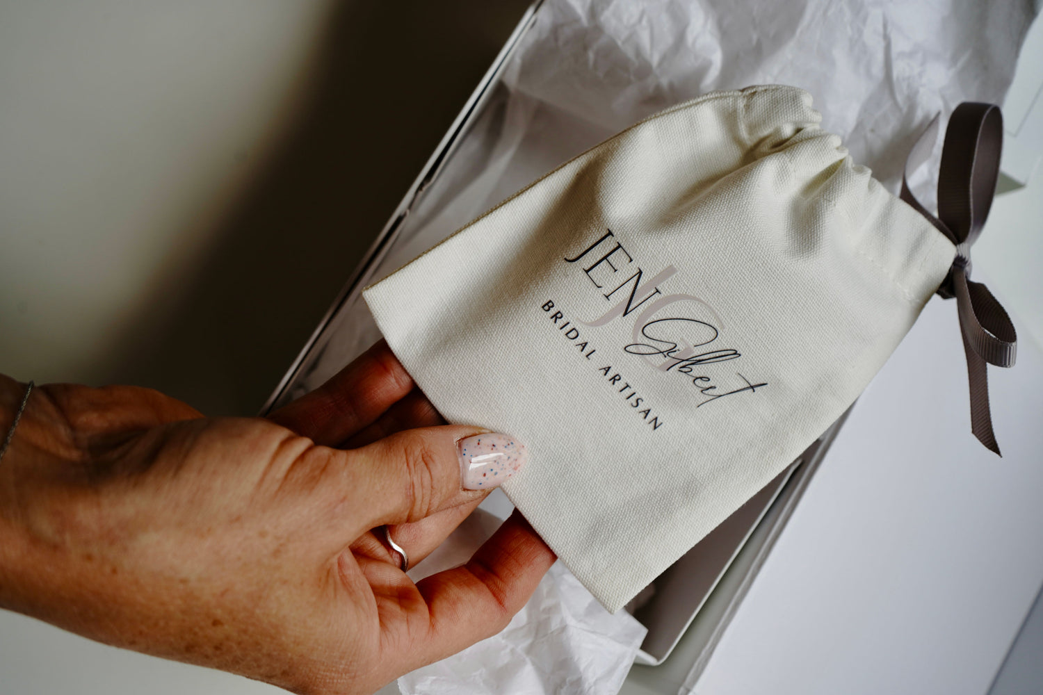 Hand holding a branded pouch with 'Jen Gilbert' on a white background
