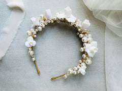 Hand wired bridal headband made with pearls, crystals and hand sculpted clay flowers, resting on a textures surface with a bridal veil in the background